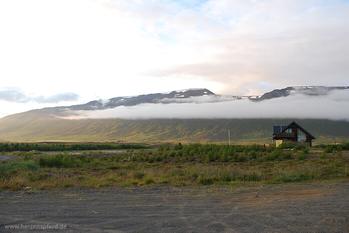 Isländisches Haus auf der Ebene, im Hintergrund das wolkenverhangene Hochland