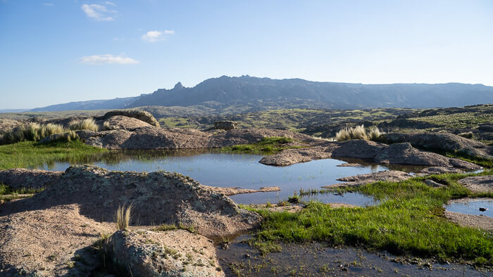 Ein kleiner Teich zwischen Felsbrocken, im Hintergrund eine Bergkette, die wie ein schlafender Riese aussieht.